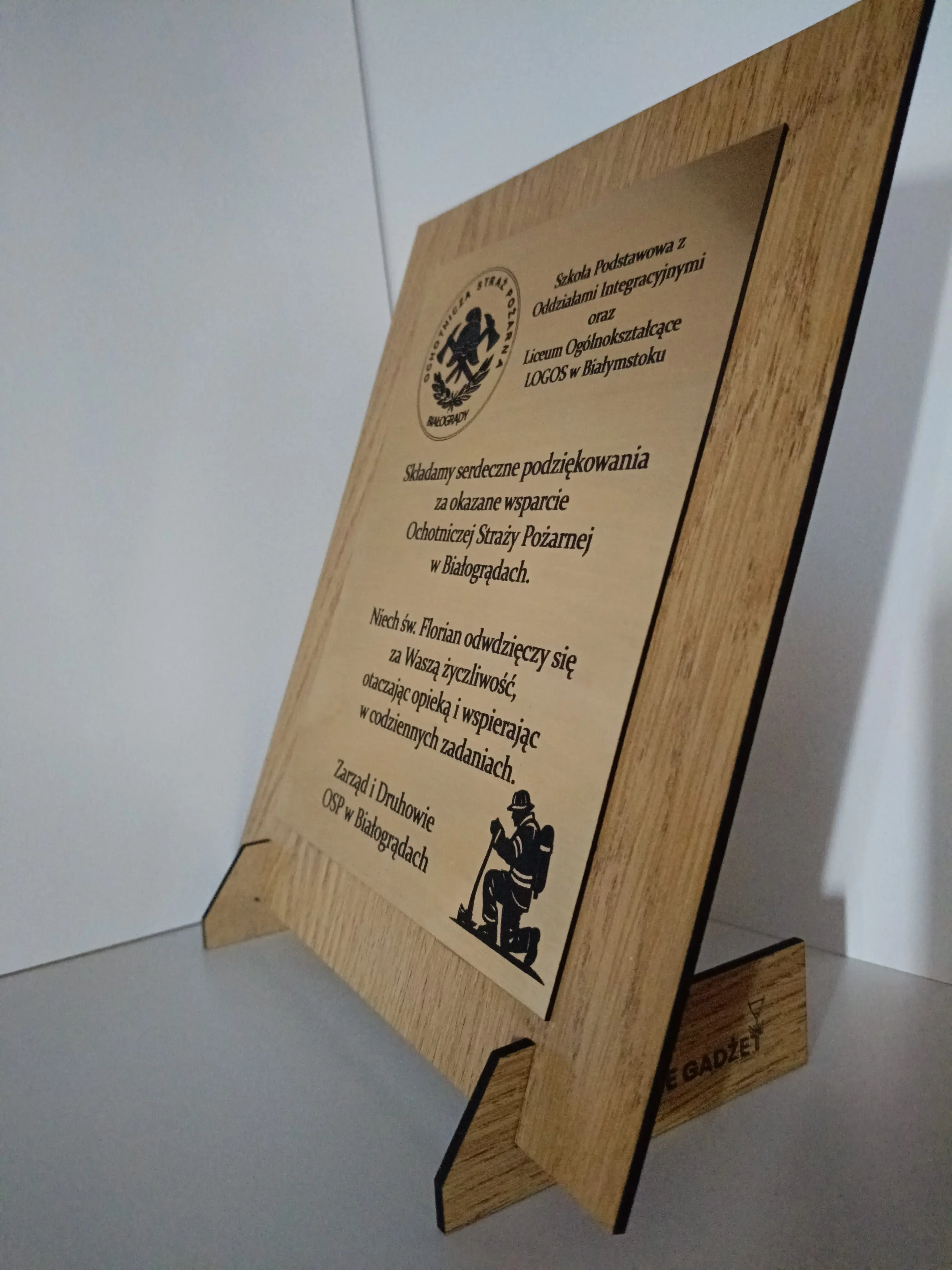 Drewniana tablica pamiątkowa na stojaku z grawerem i logotypem OSP Białogrądy, z dedykacją i grafiką strażacką