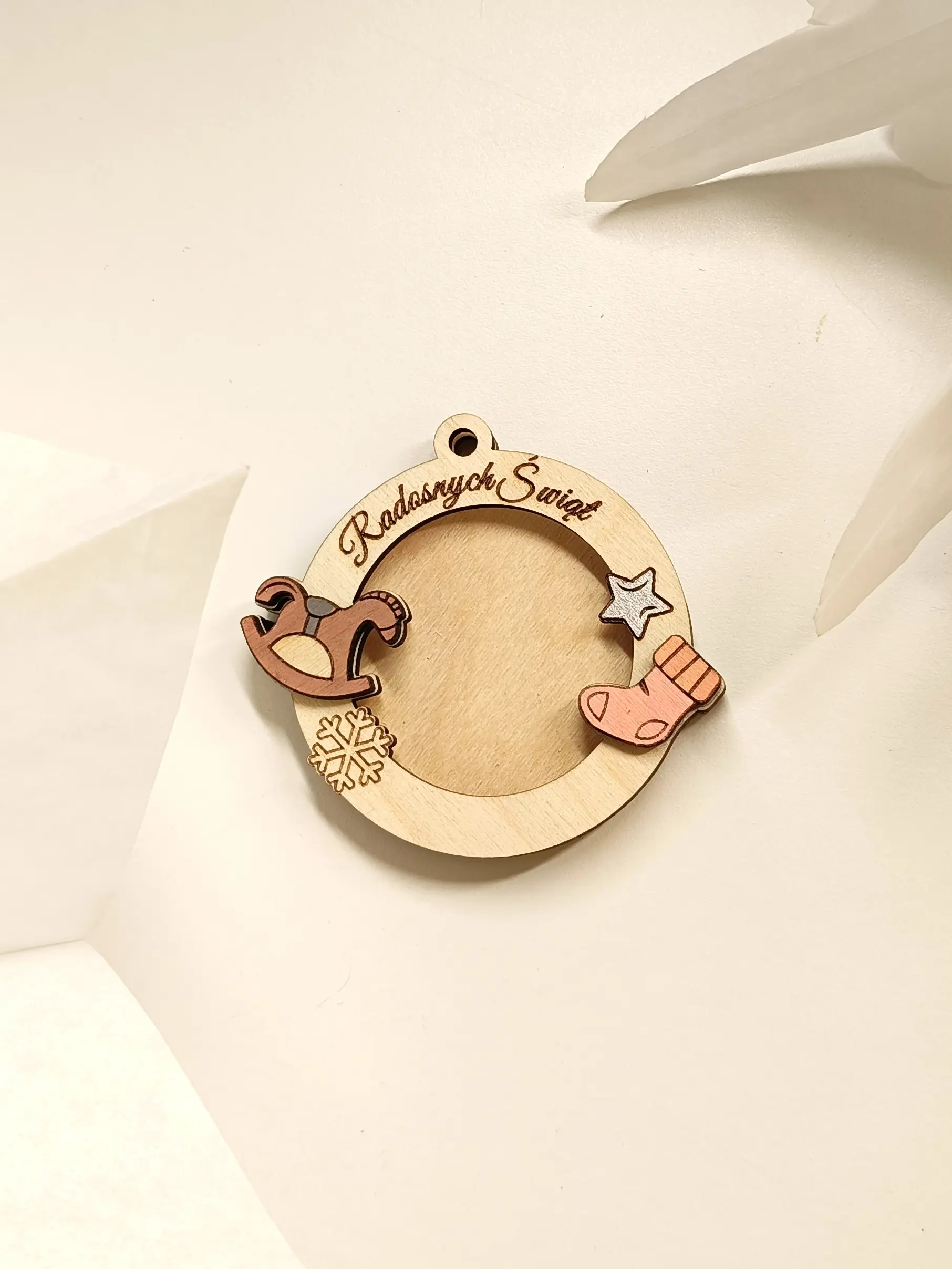 Drewniana bombka świąteczna z grawerem Radosnych Świąt, ozdobiona konikiem na biegunach, gwiazdką, skarpetą i śnieżynką