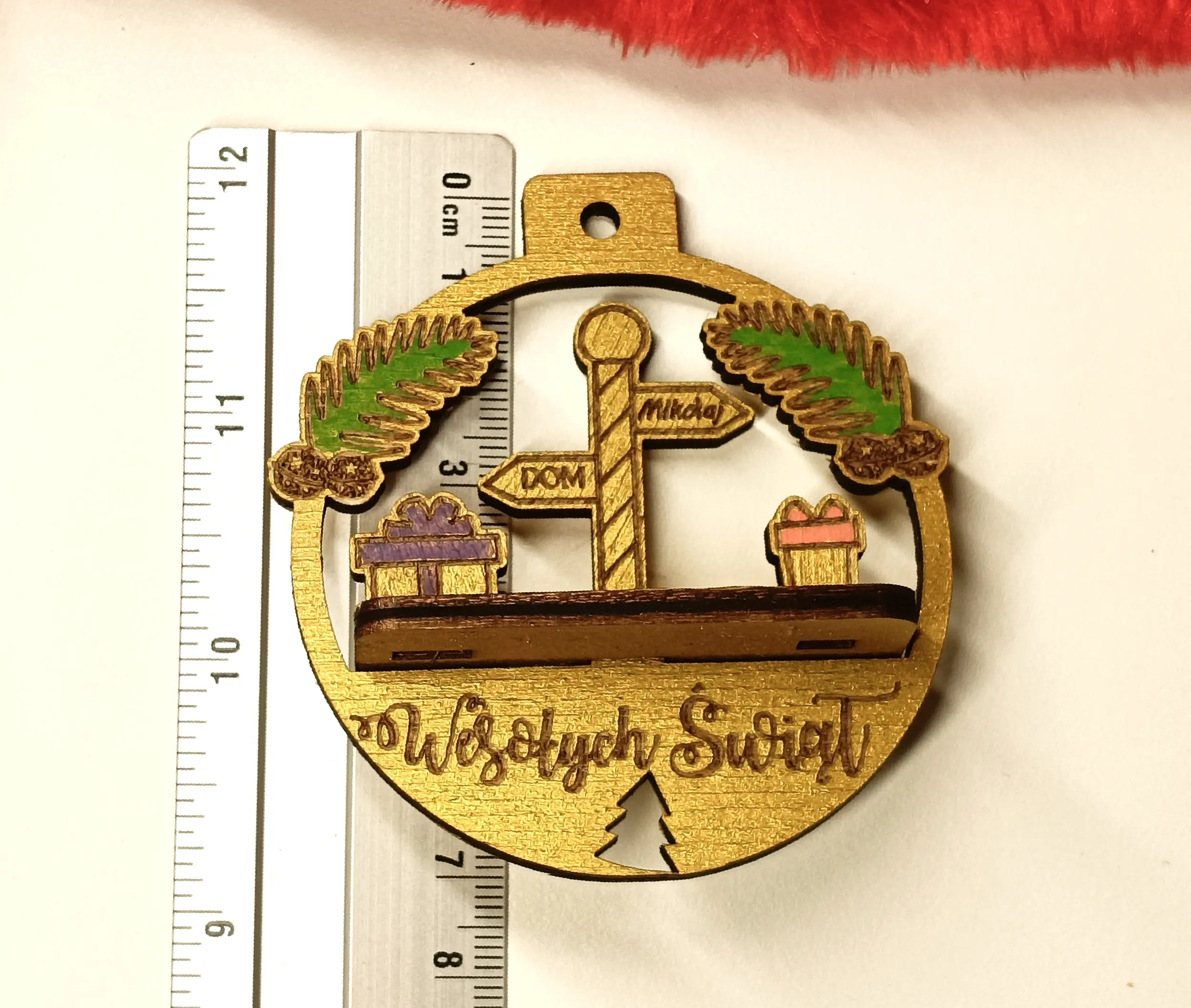 Drewniana bombka świąteczna z grawerem Wesołych Świąt, ozdobiona drogowskazem DOM, Mikołajem, prezentami i gałązkami sosny