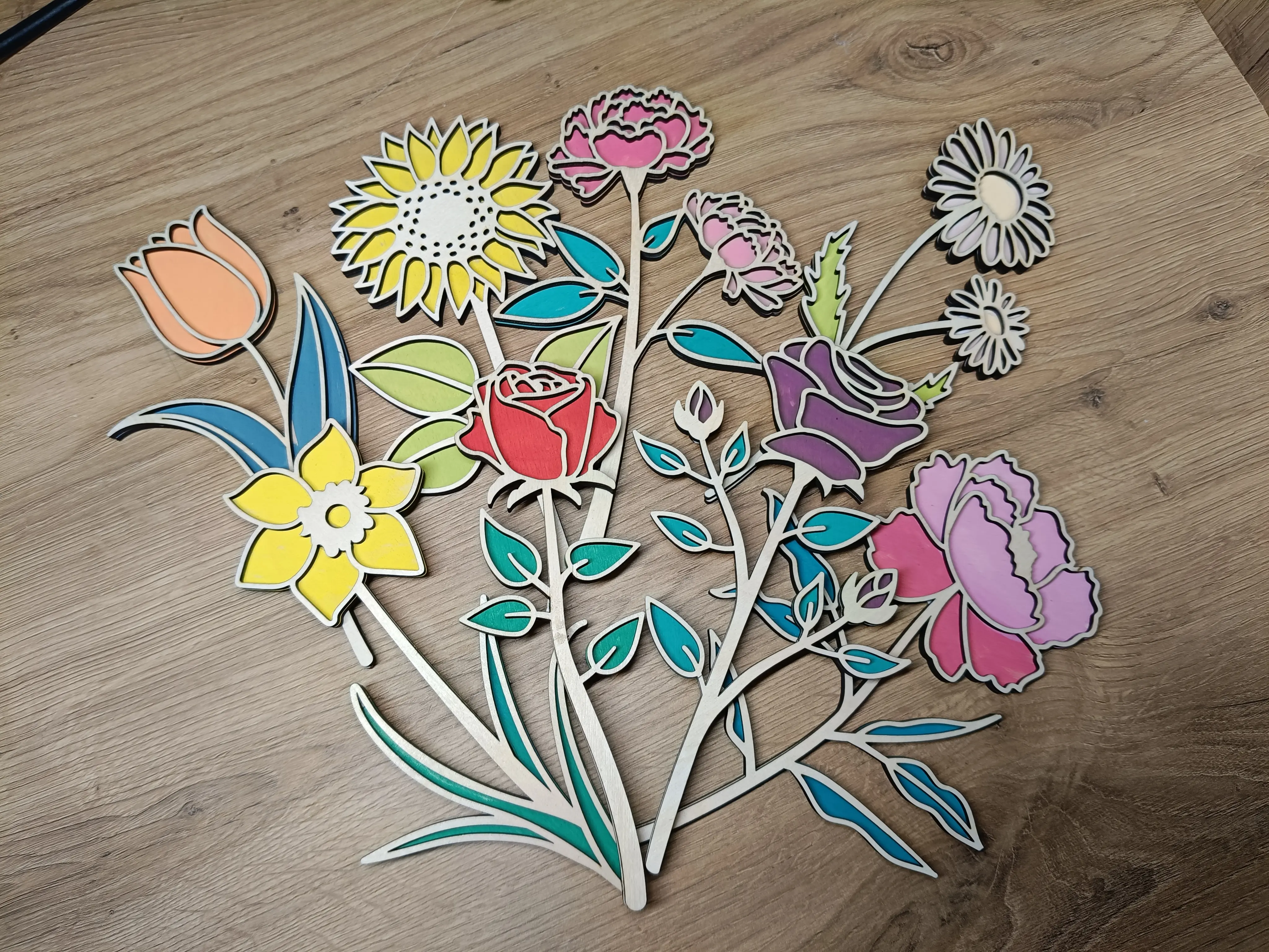 Kolorowe wycinanki kwiatowe: słoneczniki, róże, tulipany i stokrotki ułożone na drewnianym tle