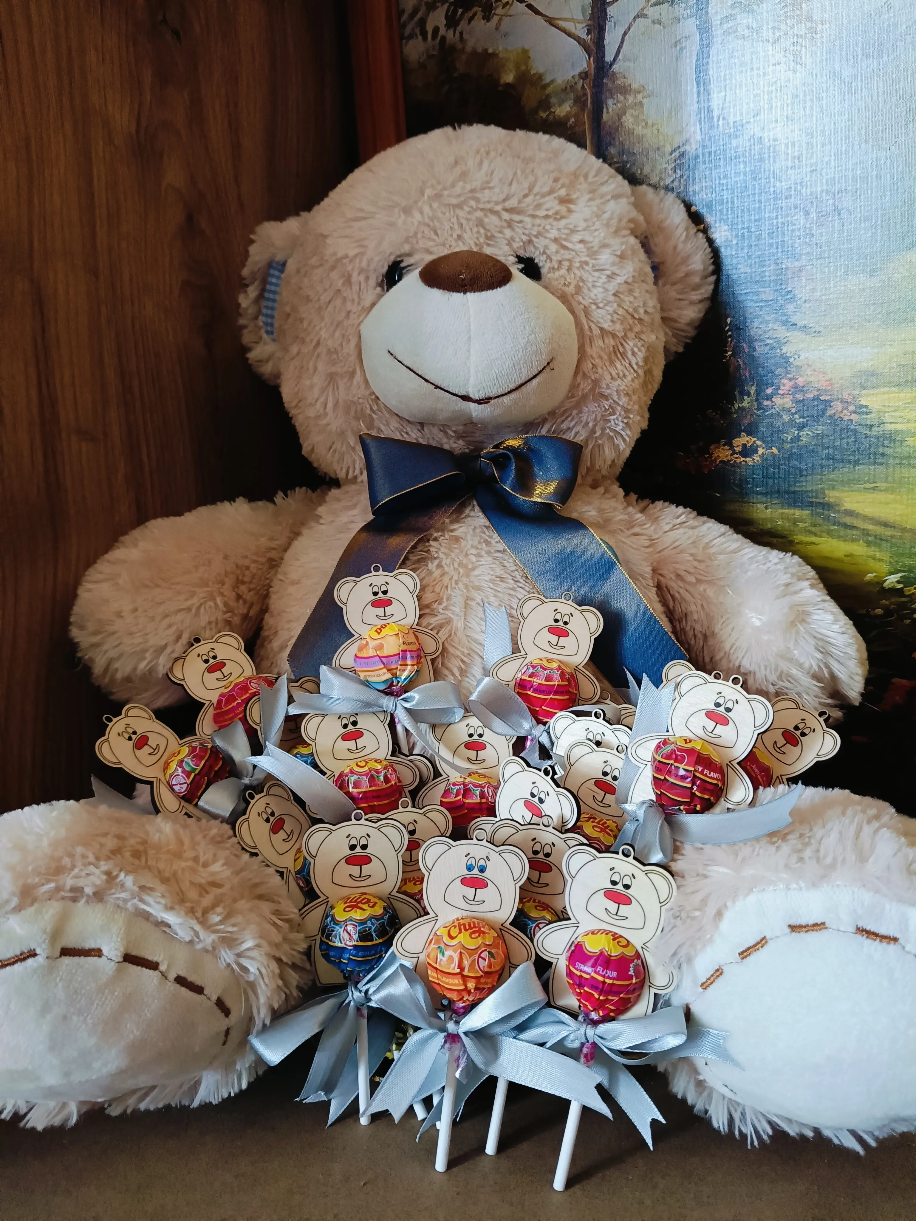 Pluszowy miś z niebieską wstążką trzymający bukiet lizaków ozdobionych buźkami misiów