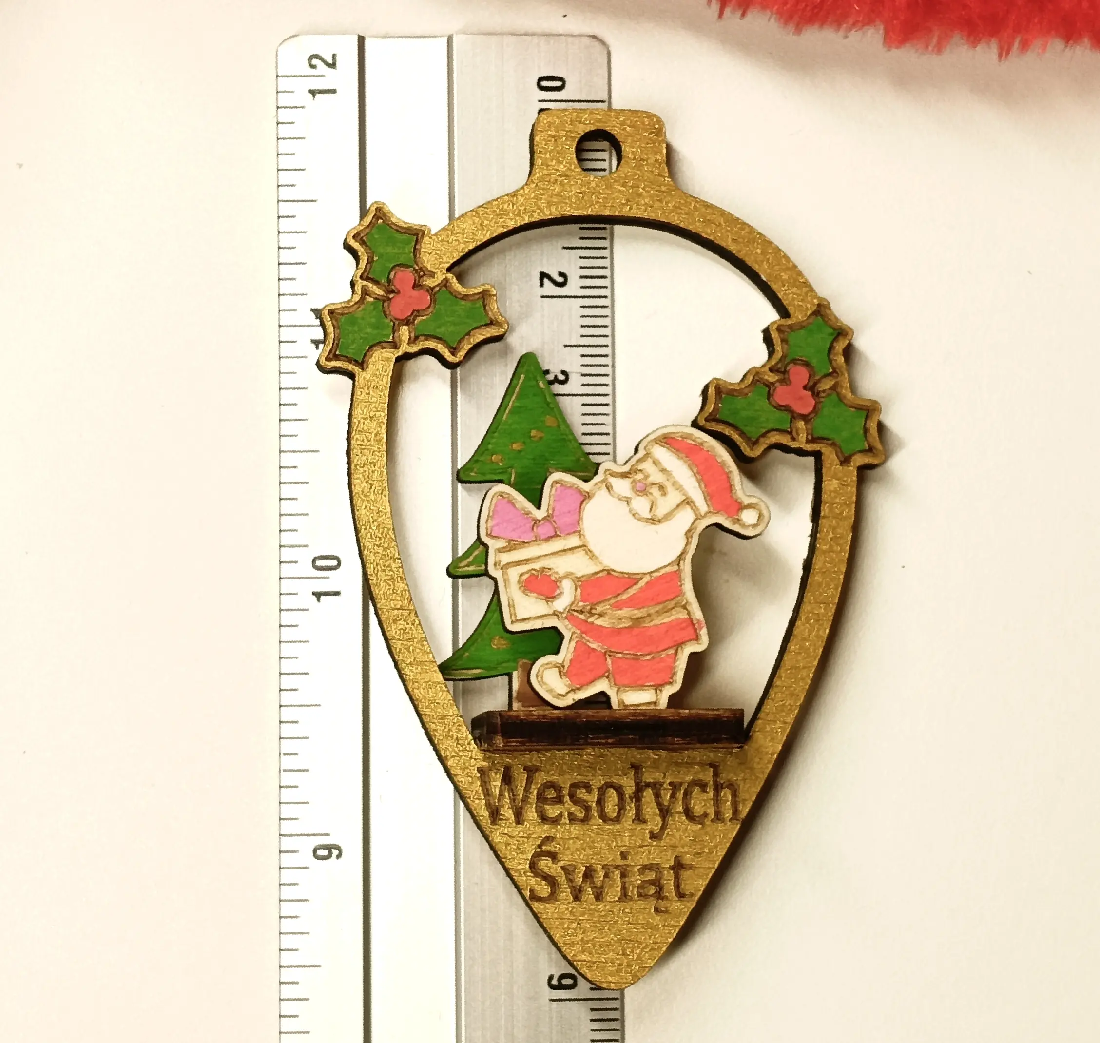 Drewniana bombka świąteczna w kształcie łezki z grawerem Wesołych Świąt, ozdobiona Mikołajem, choinką i ostrokrzewem